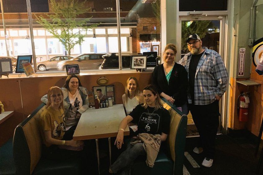 A group of people seated at a table inside a restaurant with a window view. 2