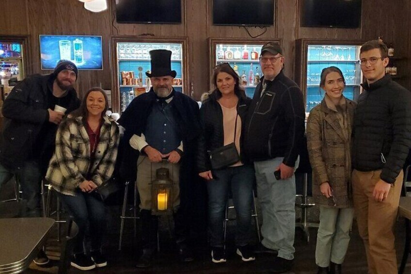 A group of people posing in a bar with shelves of bottles and a television screen in the background. 5