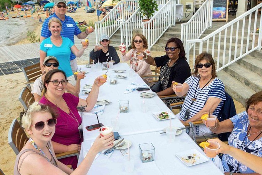 A group of people dining at an outdoor table with a beach in the background. 4