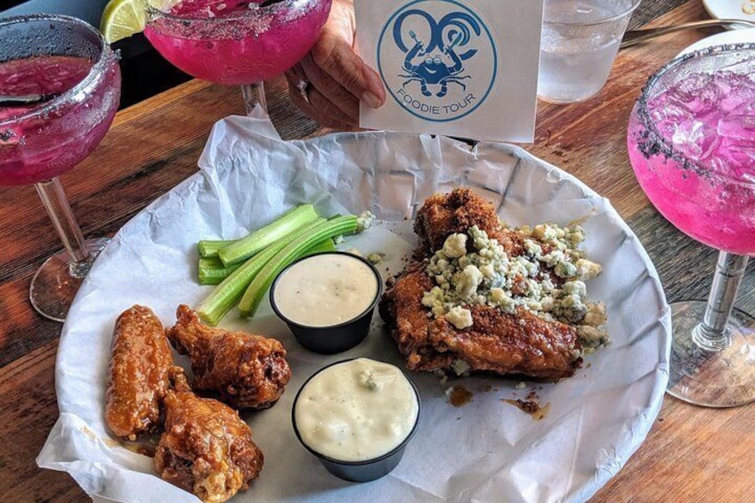 A plate of fried chicken wings, a piece of chicken with blue cheese, celery, and two dipping sauces on a wooden table. 2