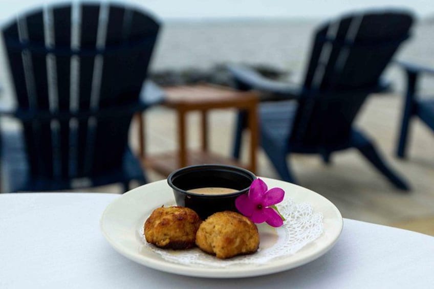 Un plato con dos alimentos fritos y una taza de café sobre una mesa, con vista a la playa al fondo. 2