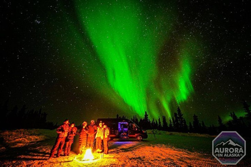Un groupe de personnes se tient près d’un feu de camp, sous les aurores boréales. 4