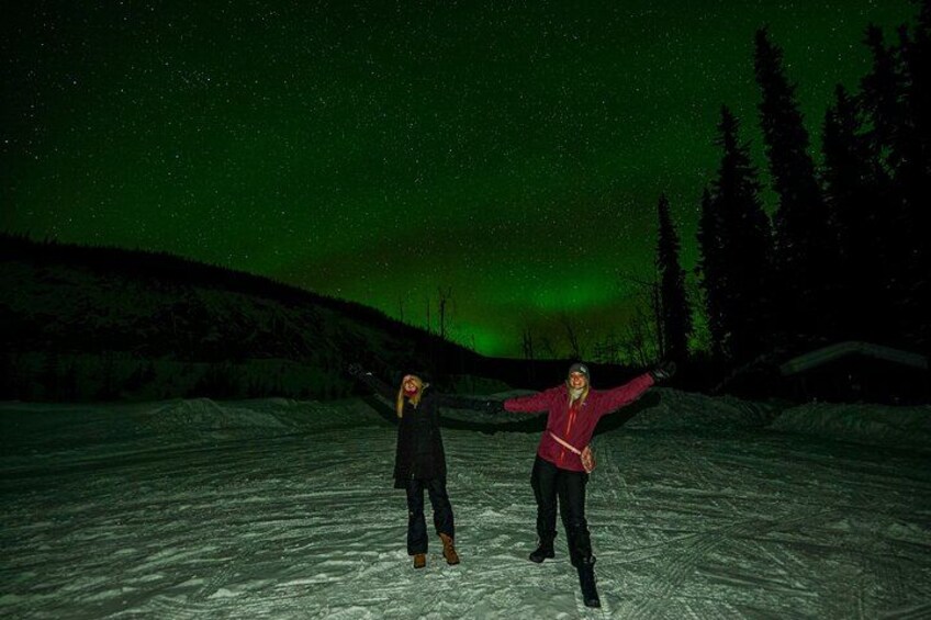 Deux personnes se tiennent sur un sol enneigé, et une aurore boréale verte illumine le ciel. 2