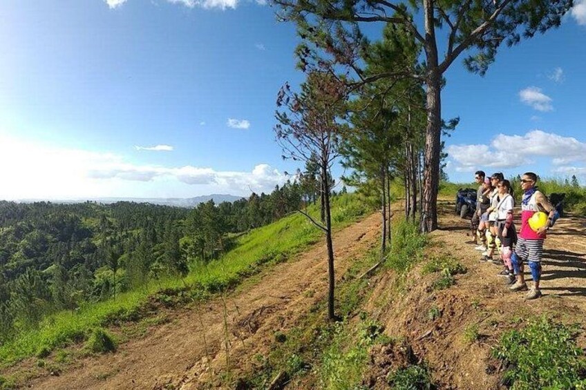 A group of people hiking on a dirt trail with a forested landscape in the background. 1