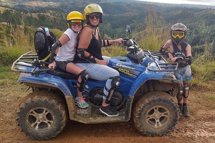 Three people on a blue ATV in a rural, hilly landscape. 2