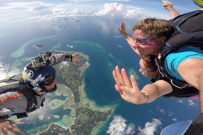 Two people skydiving over a coastal area with clear blue waters and islands below. 1