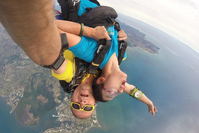 A person skydiving with a parachute, another person holding them, and a landscape below. 3
