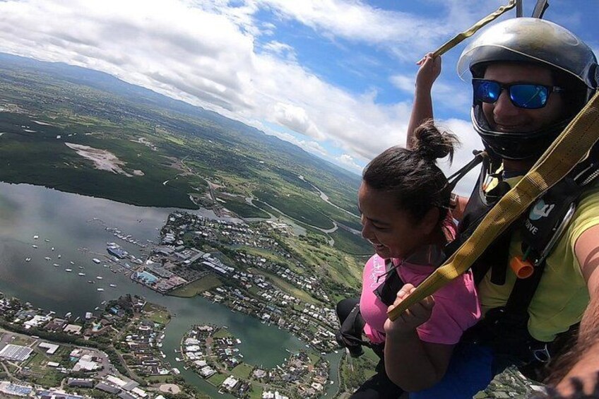A person in a harness and helmet, holding onto a safety bar, with a scenic view of a coastal town and a body of water below. 2