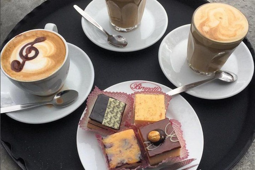 A tray with three cups of coffee, a plate with four pieces of cake, and a spoon. 4