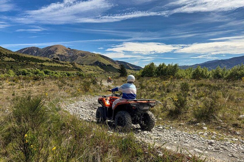 A person riding an ATV on a rocky trail surrounded by mountains and vegetation. 3