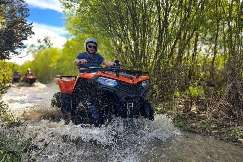 A person riding an ATV on a muddy path surrounded by greenery. 1