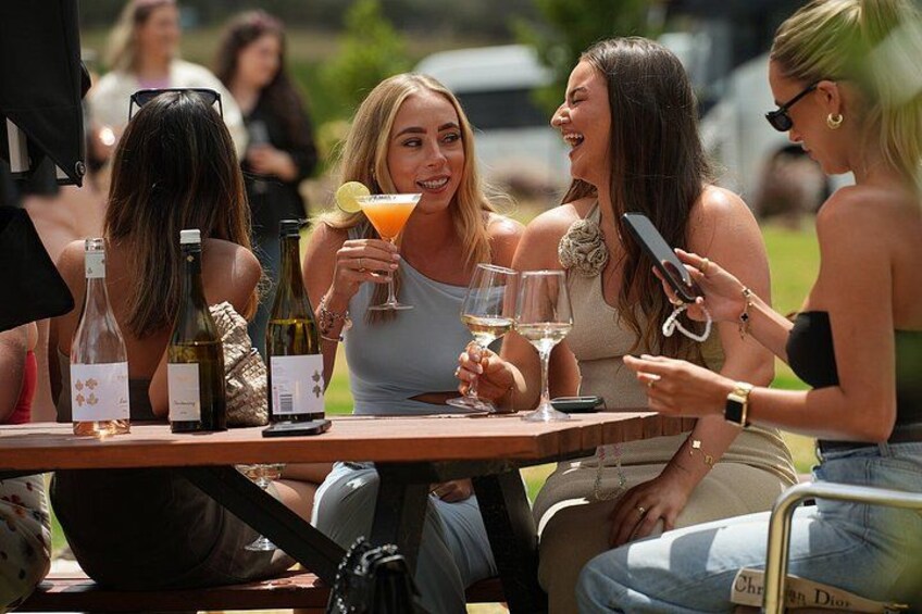 A group of people sitting at an outdoor table with bottles and glasses. 4