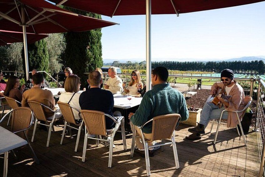 People sitting at tables outdoors, with a view of a vineyard and hills in the background. 5