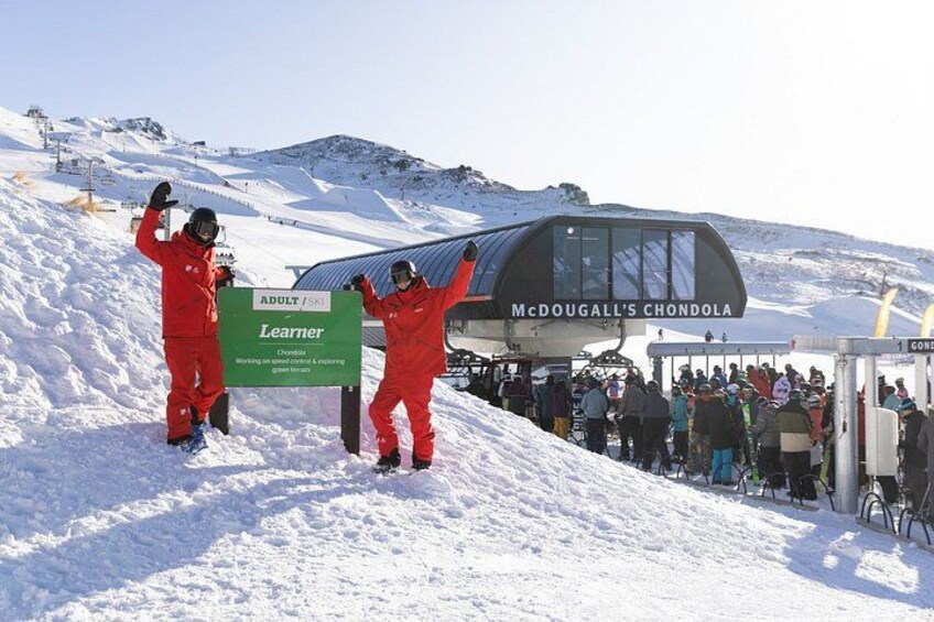 Un télésiège avec des personnes à bord, un panneau indiquant le « McDougall's Chondola », et un paysage montagneux enneigé. 1