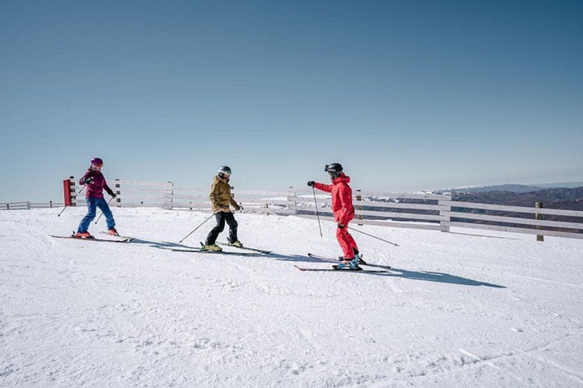 Trois skieurs sur une pente enneigée, sous un ciel dégagé, avec des montagnes qui se dessinent à l'horizon. 5