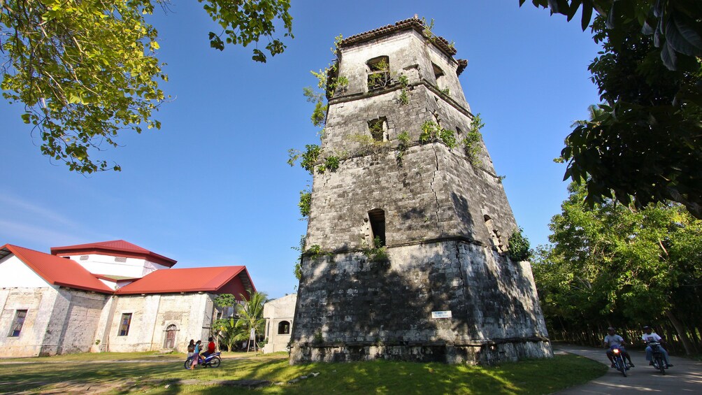 A historic stone tower with a red roof, surrounded by lush greenery and a clear blue sky. 3