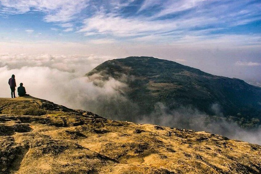 A mountainous landscape with two people standing on a rocky outcrop, overlooking a valley shrouded in mist. 3