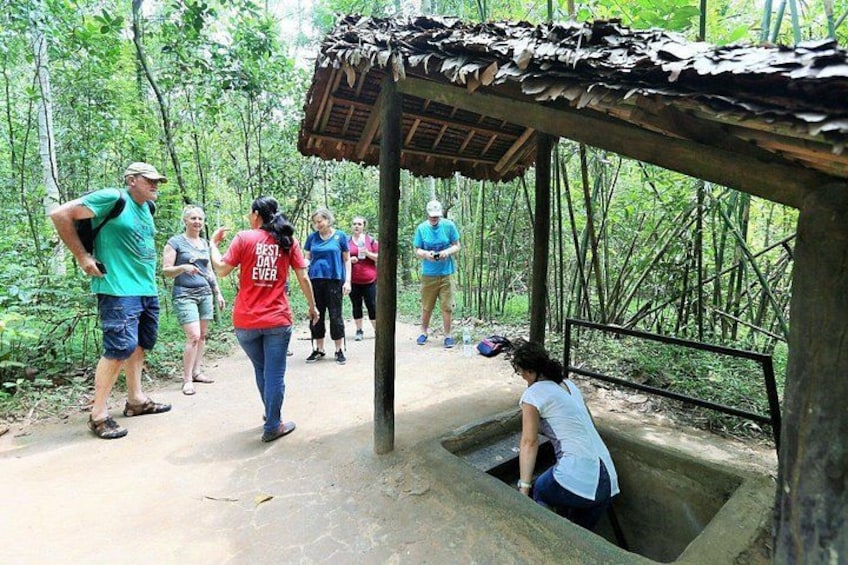 A group of people standing under a thatched roof structure in a forested area. 4