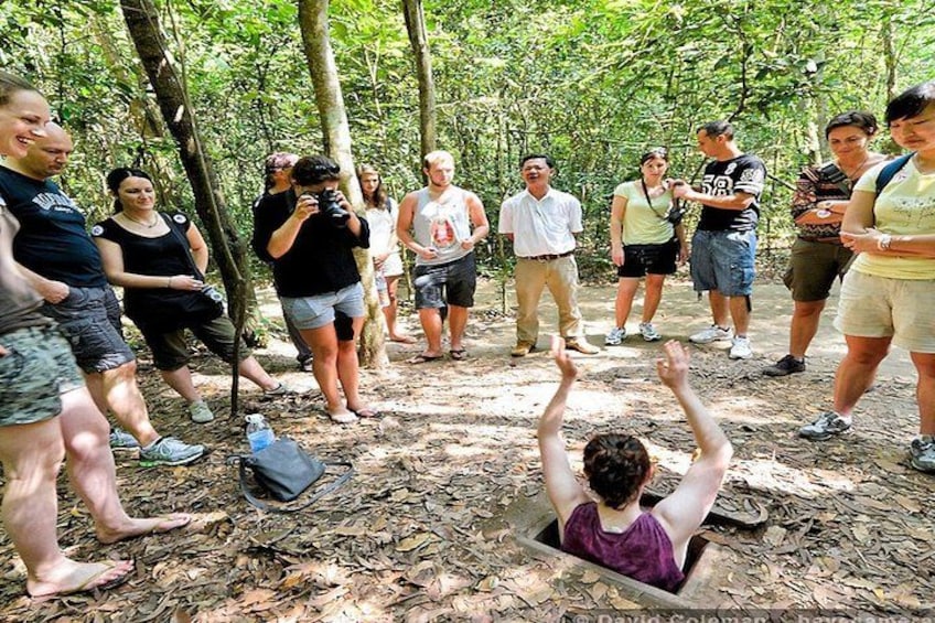 A group of people in a forested area, some standing and others sitting in a dug-out area. 1