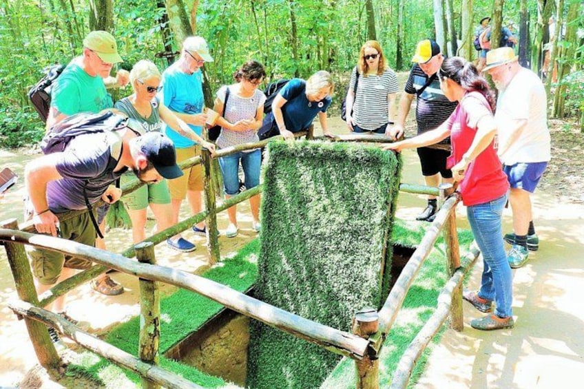 A group of people standing around a wooden structure with a green surface, possibly a bridge or platform, in a forested area. 3