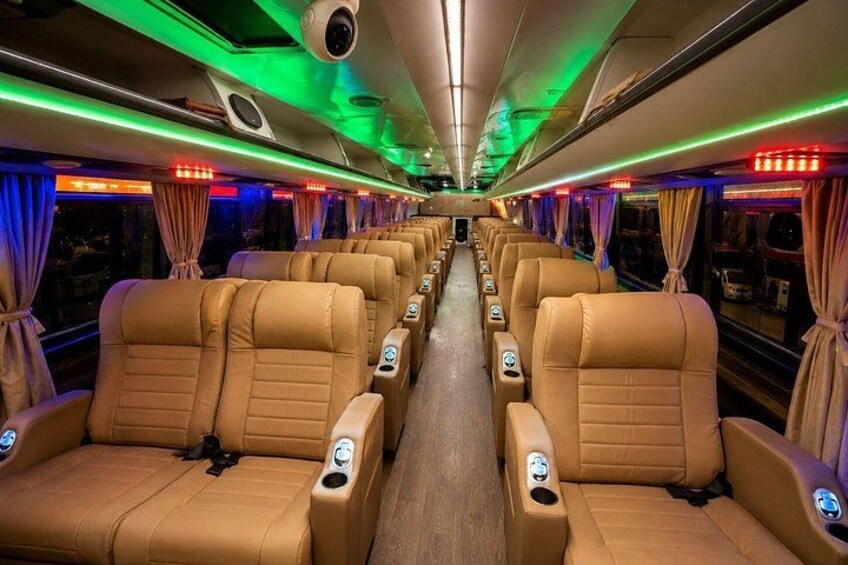 A train interior with rows of beige leather seats, overhead luggage compartments, and green and red lighting. 3