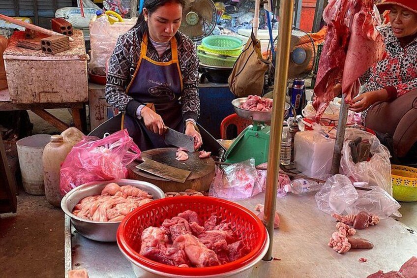 A person preparing food at a market stall with various meats and kitchen tools. 3