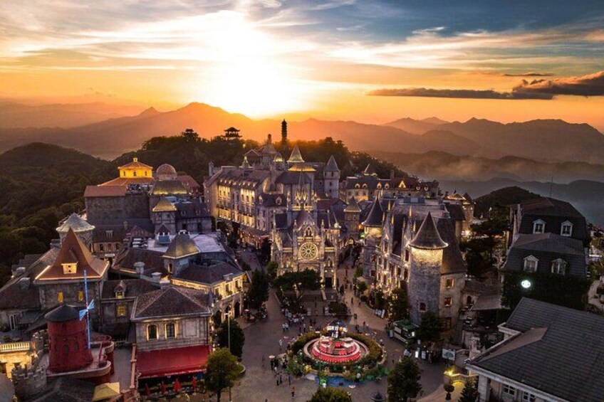 Un ensemble de bâtiments évoquant un château, avec de nombreuses tours et une cour centrale, entouré de montagnes et se détachant sur le ciel au coucher du soleil. 2