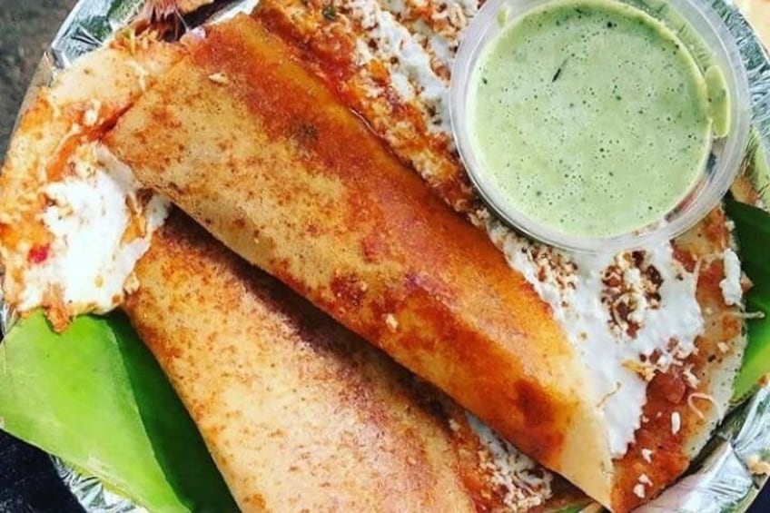 Crepe enrollada con crema blanca y salsa verde, servida sobre una hoja de plátano. 3