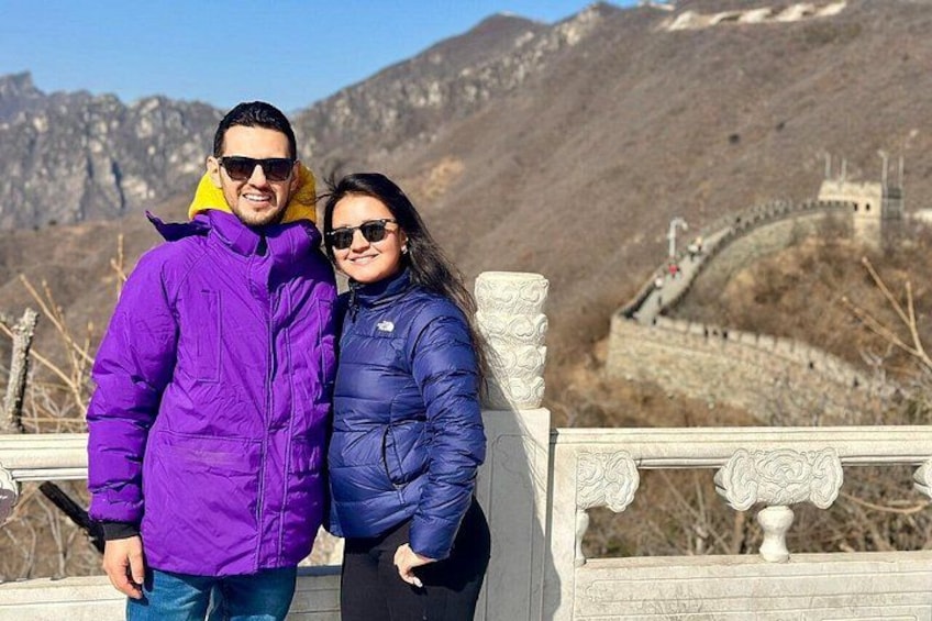 Two people standing on a bridge with a mountainous landscape and the Great Wall of China in the background. 1