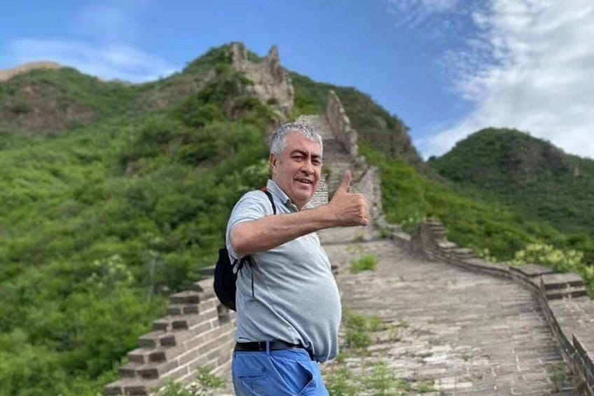 A person giving a thumbs-up gesture in front of a historical stone pathway with lush green hills in the background. 5