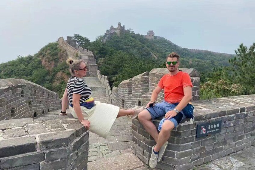Deux personnes assises sur la Grande Muraille de Chine, avec un paysage montagneux en arrière-plan. 1