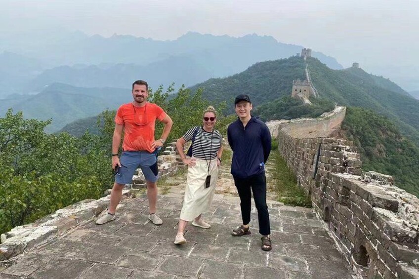 Trois personnes se tiennent sur la Grande Muraille de Chine, avec un paysage montagneux en arrière-plan. 3