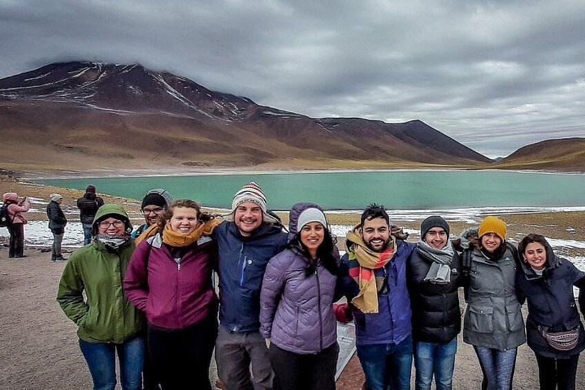 A group of people standing in front of a lake with mountains in the background. 1