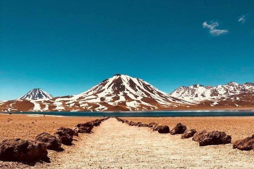 A mountain range with a clear sky, a dirt path leading towards the mountains, and a body of water in the foreground. 5