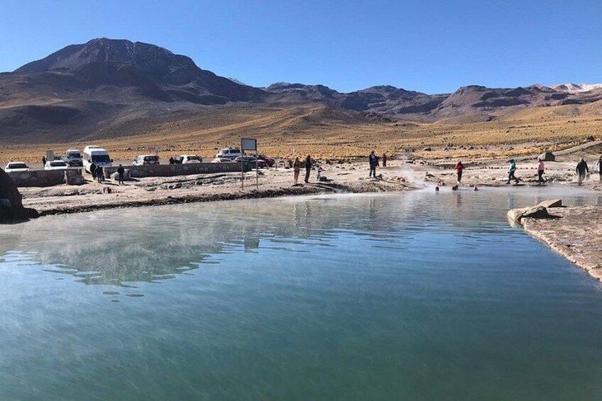 A geothermal area with a pool of water, vehicles, and people. 4