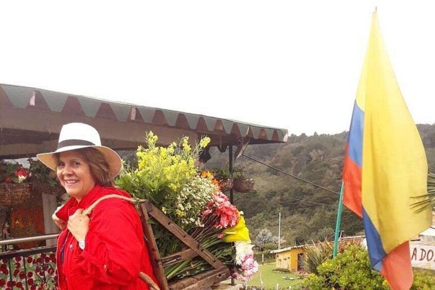 A person in a red jacket and white hat standing in front of a flower arrangement with a flag in the background. 3