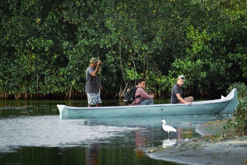 En båd med tre personer på en stille flod omgivet af frodig vegetation. 1