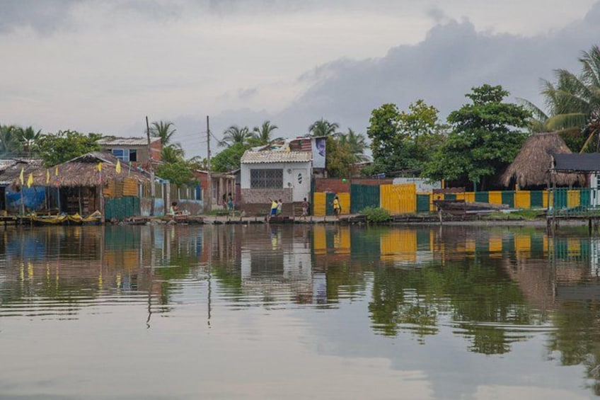 A calm river with houses reflecting on the water, a person walking, and palm trees in the background. 4