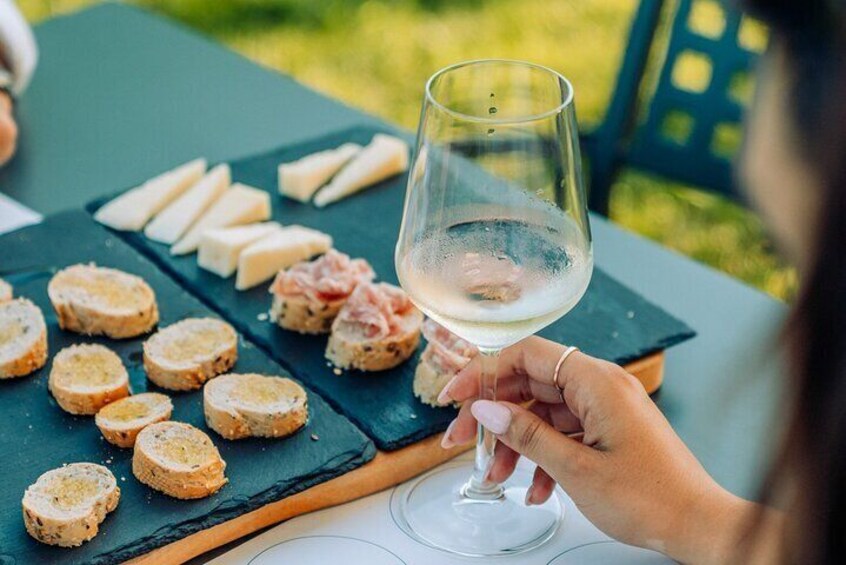 Une personne tenant un verre de vin à une table en plein air, devant une sélection de fromages et de pain. 5