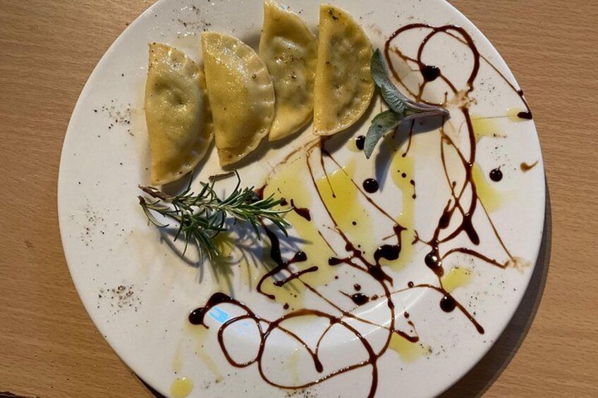 A plate with ravioli, a sprig of rosemary, and a drizzle of sauce. 4