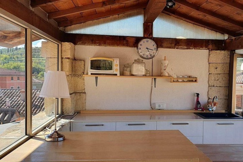 A rustic kitchen with a wooden table, a lamp, a microwave, and a clock on the wall. 1