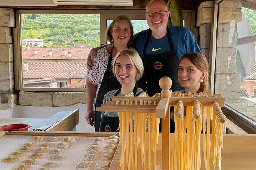 A group of people in a kitchen with pasta drying racks and a window overlooking buildings. 2