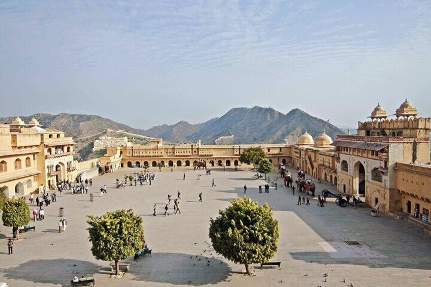 Un ampio cortile aperto con edifici storici, alberi e montagne sullo sfondo. 3
