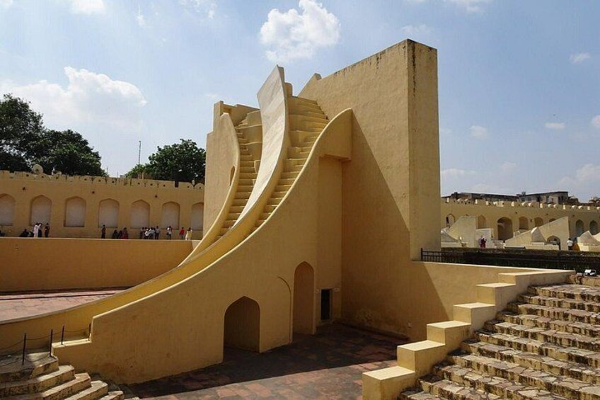 A yellow spiral staircase leading up to a building, surrounded by a courtyard with arches and steps. 4