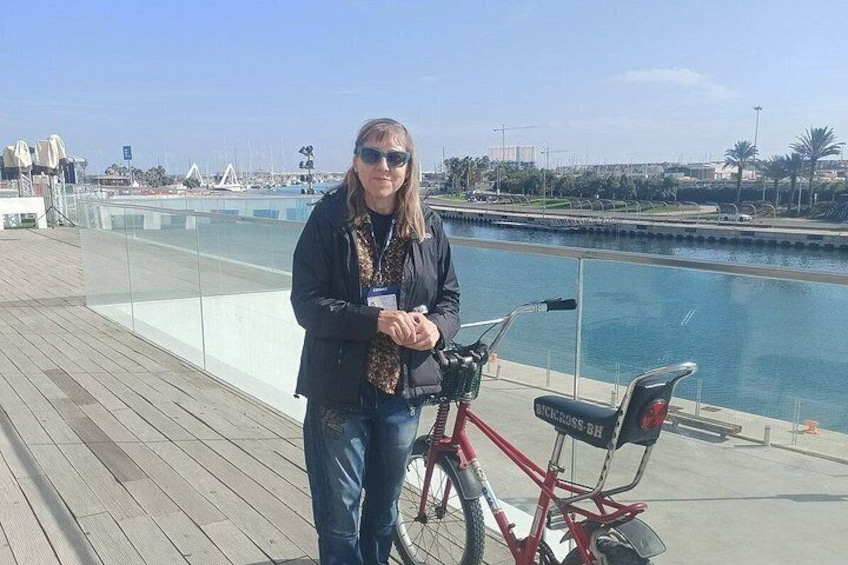 Une personne se tient à côté d’un vélo rouge sur une terrasse en bois, au bord de l’eau. 2