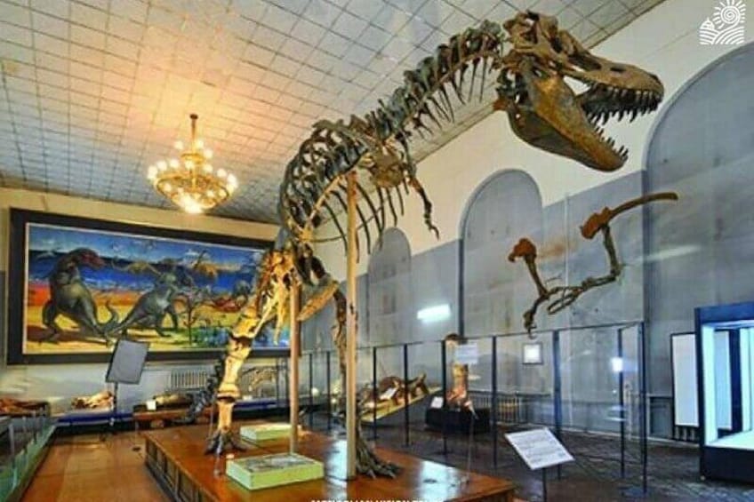 A dinosaur skeleton exhibit in a museum with a painting in the background. 3