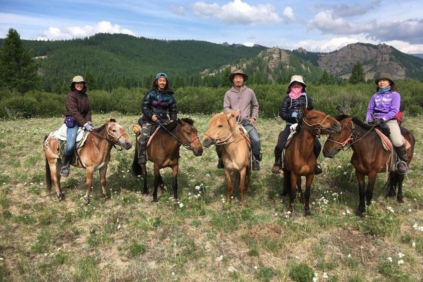 Cinco personas a caballo en un campo cubierto de hierba, con montañas al fondo. 4