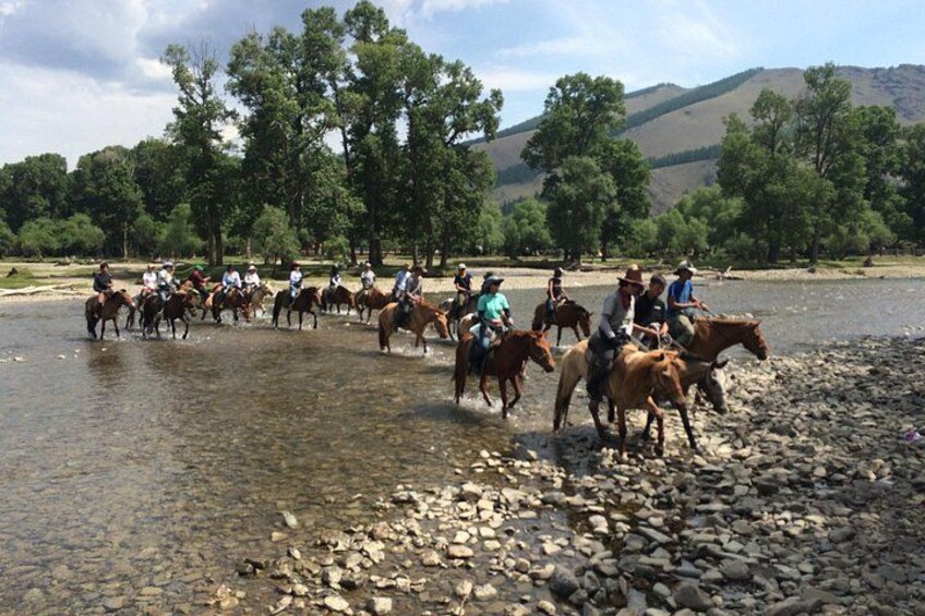 Eine Gruppe von Menschen reitet auf Pferden entlang eines Flussufers. 1