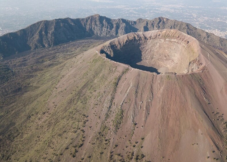 A volcanic crater surrounded by rugged terrain and distant cityscape. 1