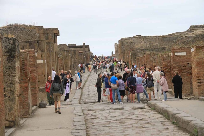 A crowded ancient Roman street with stone walls and a cobblestone path. 3